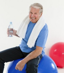 senior adult sitting on fitness ball in gym and holding water bottle